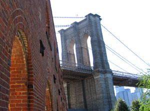 The Brooklyn Bridge and the arched brick wall of an historic structure in the park.